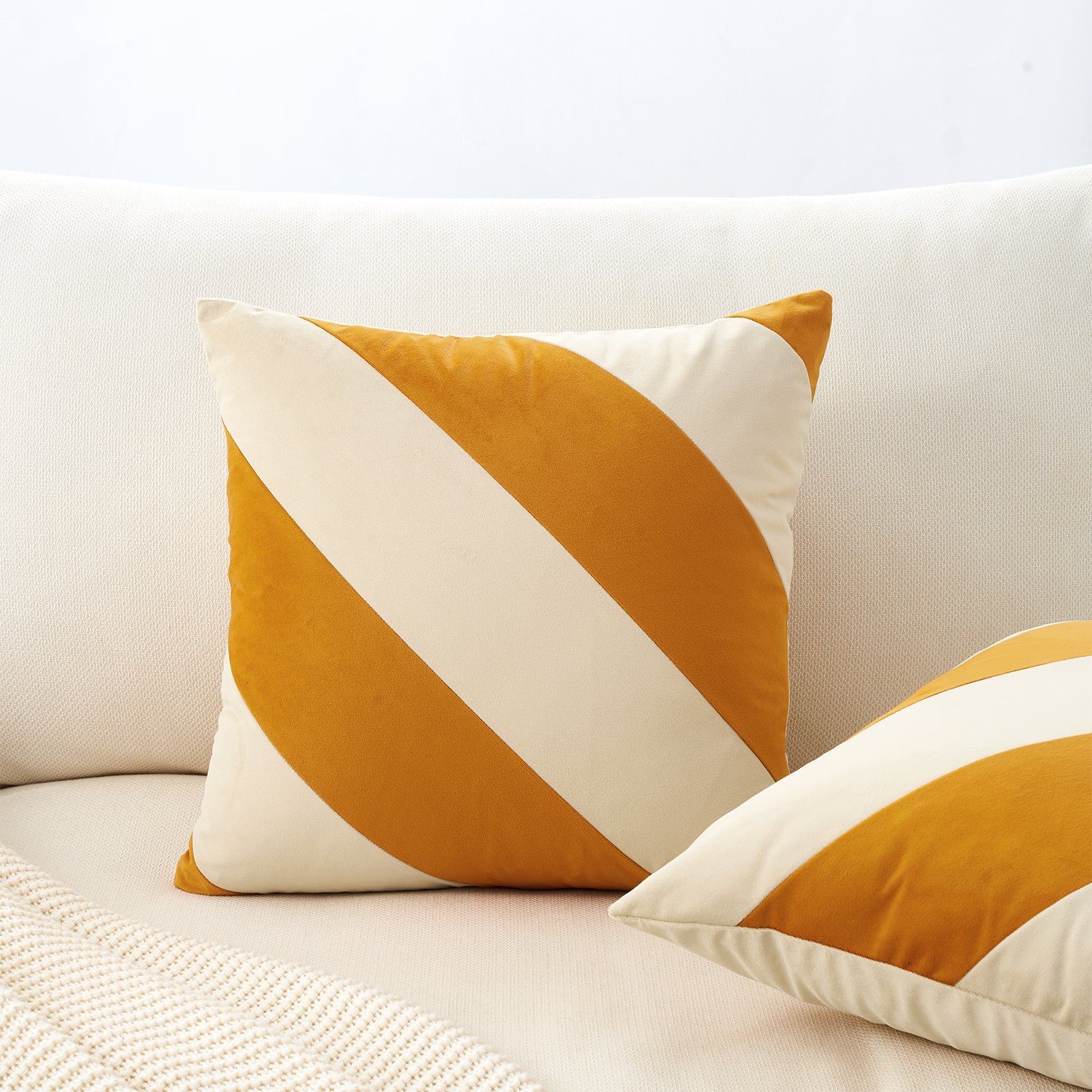 Two decorative pillows with orange and white stripes on a light-colored sofa.