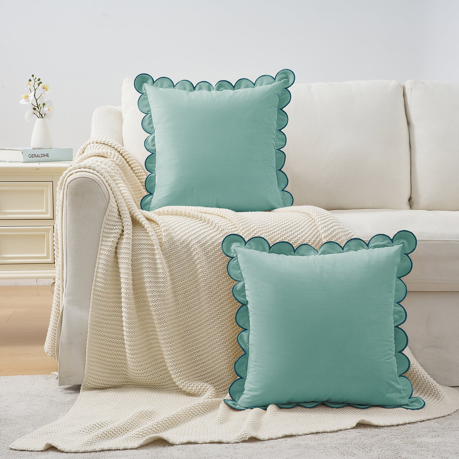 Two turquoise pillows with scalloped edges on a beige couch with a white blanket.