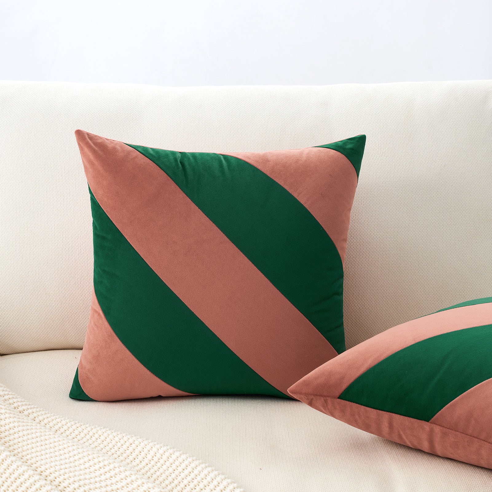 Two decorative pillows with green and pink stripes on a white couch.