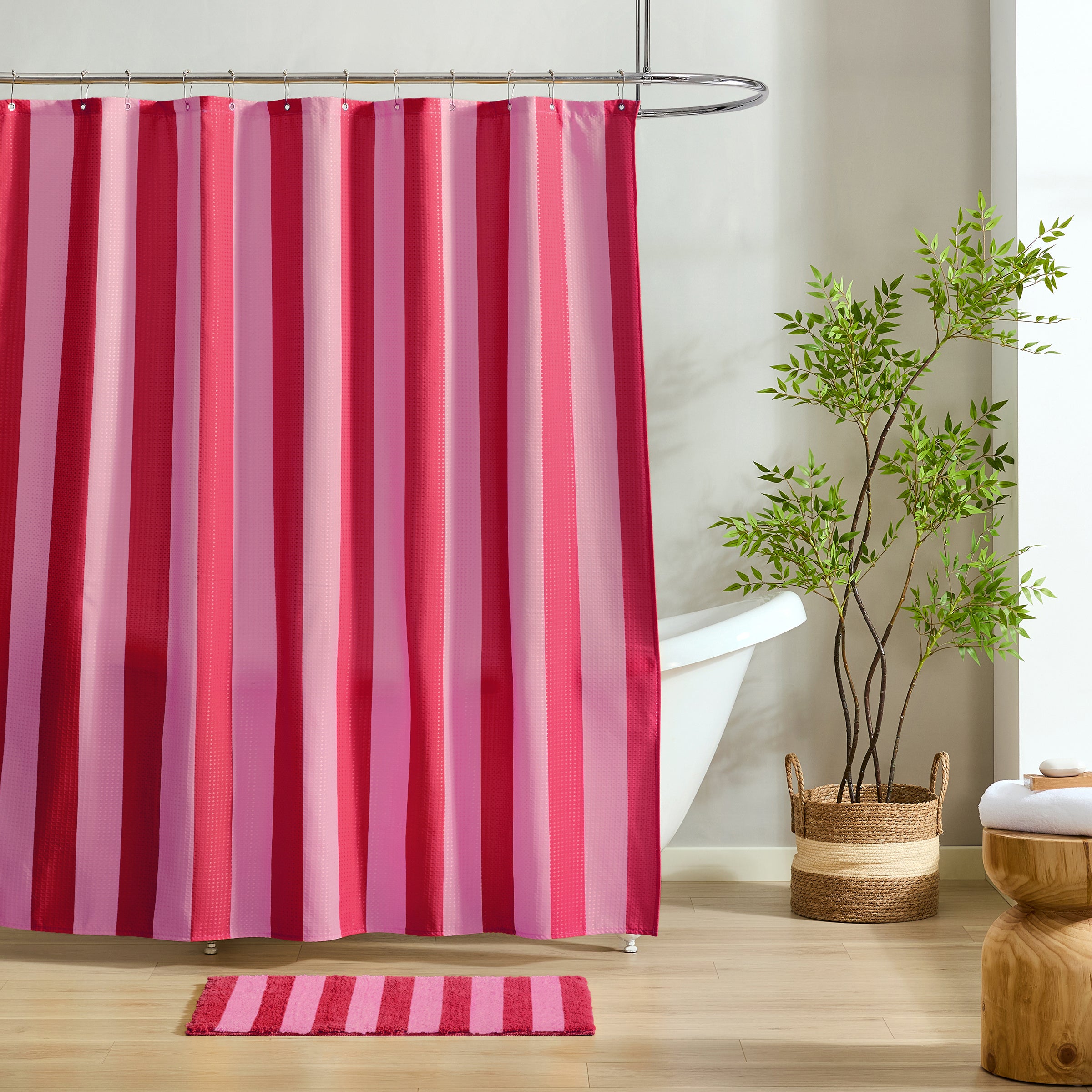 Striped pink and red shower curtain with a plant and rug in a bathroom setting