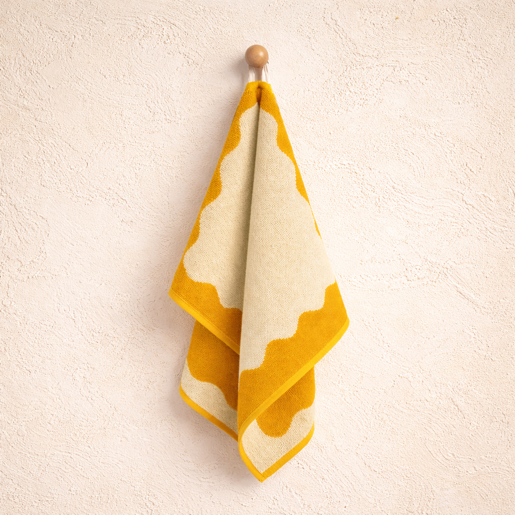 Yellow and white patterned towel hanging on a wooden hook against a beige wall.