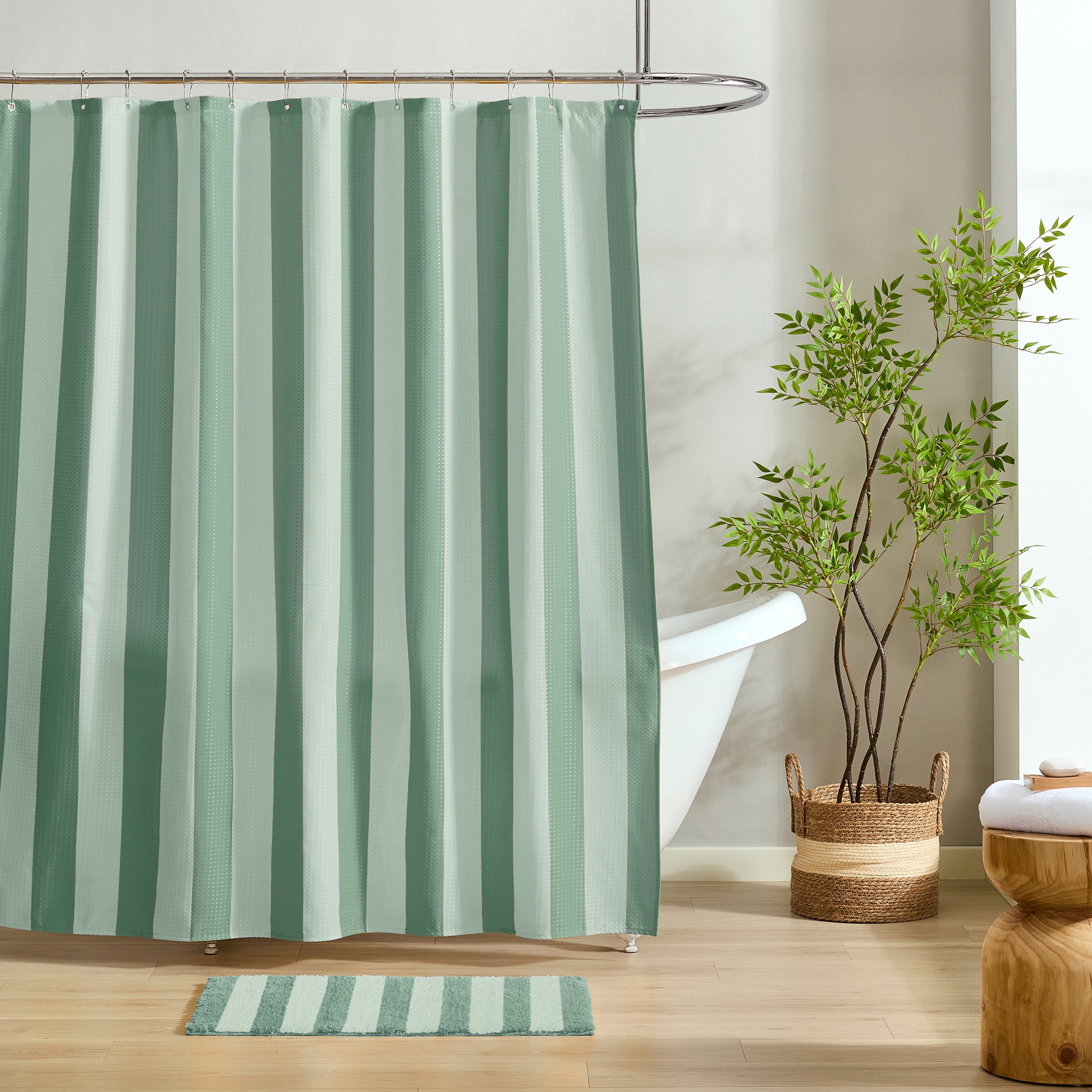 A mint green and white striped shower curtain hanging in a bright bathroom, with a white tub, a potted green plant in a woven basket, a striped bath mat, and a wooden stool visible.