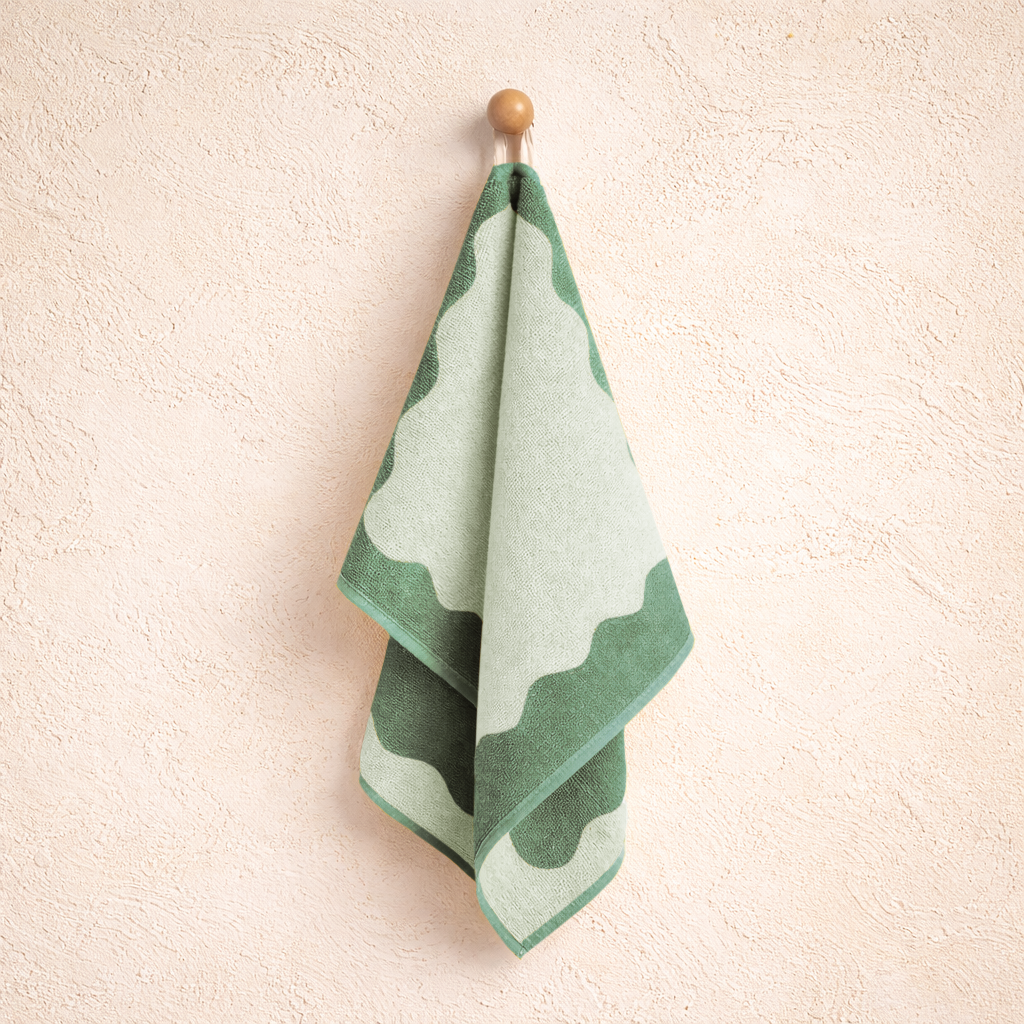 Green and white patterned towel hanging on a wooden hook against a beige wall.