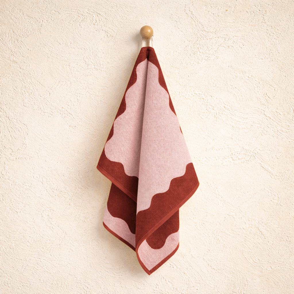 Decorative towel with wavy pattern in red and pink on a beige wall.