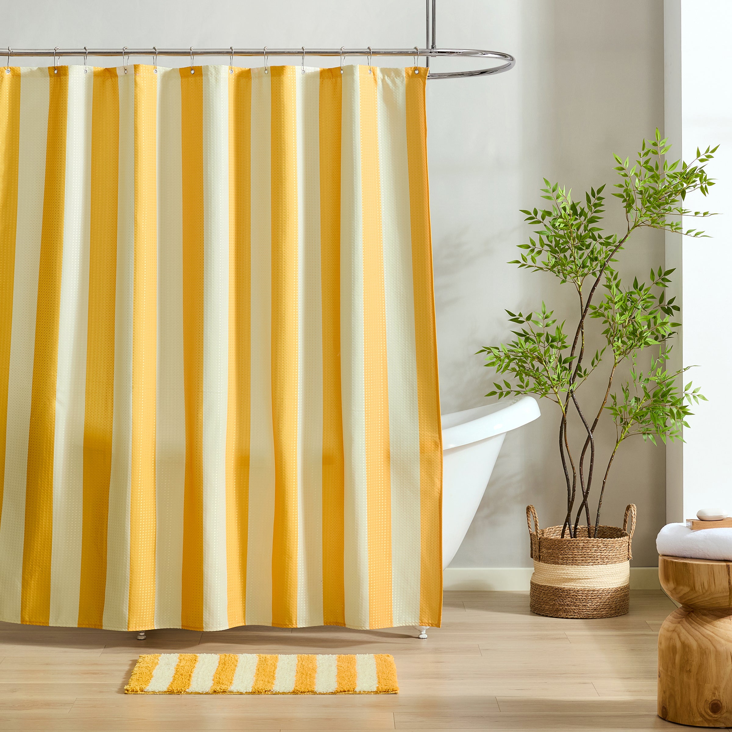 Yellow and white striped shower curtain in a bathroom with a plant and rug.