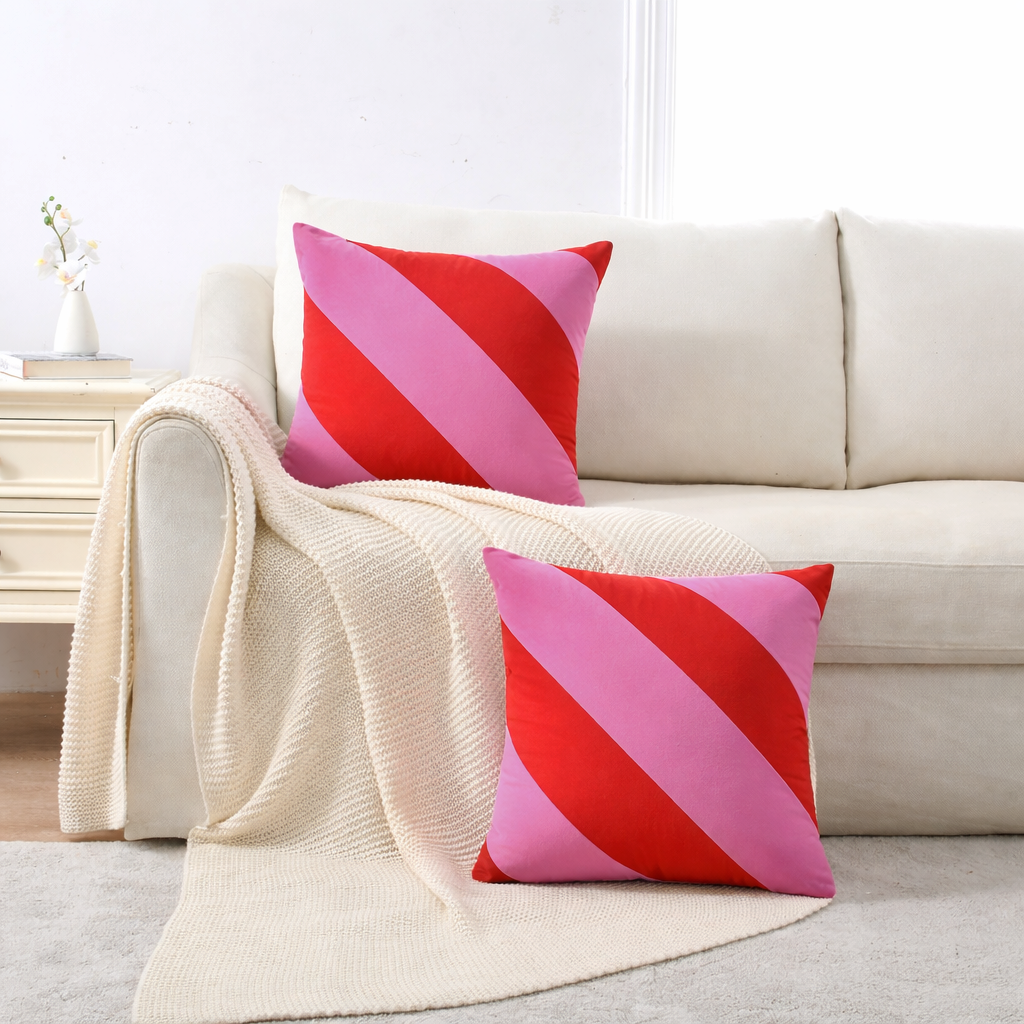 Pink and red striped pillows on a beige sofa with a white wall background