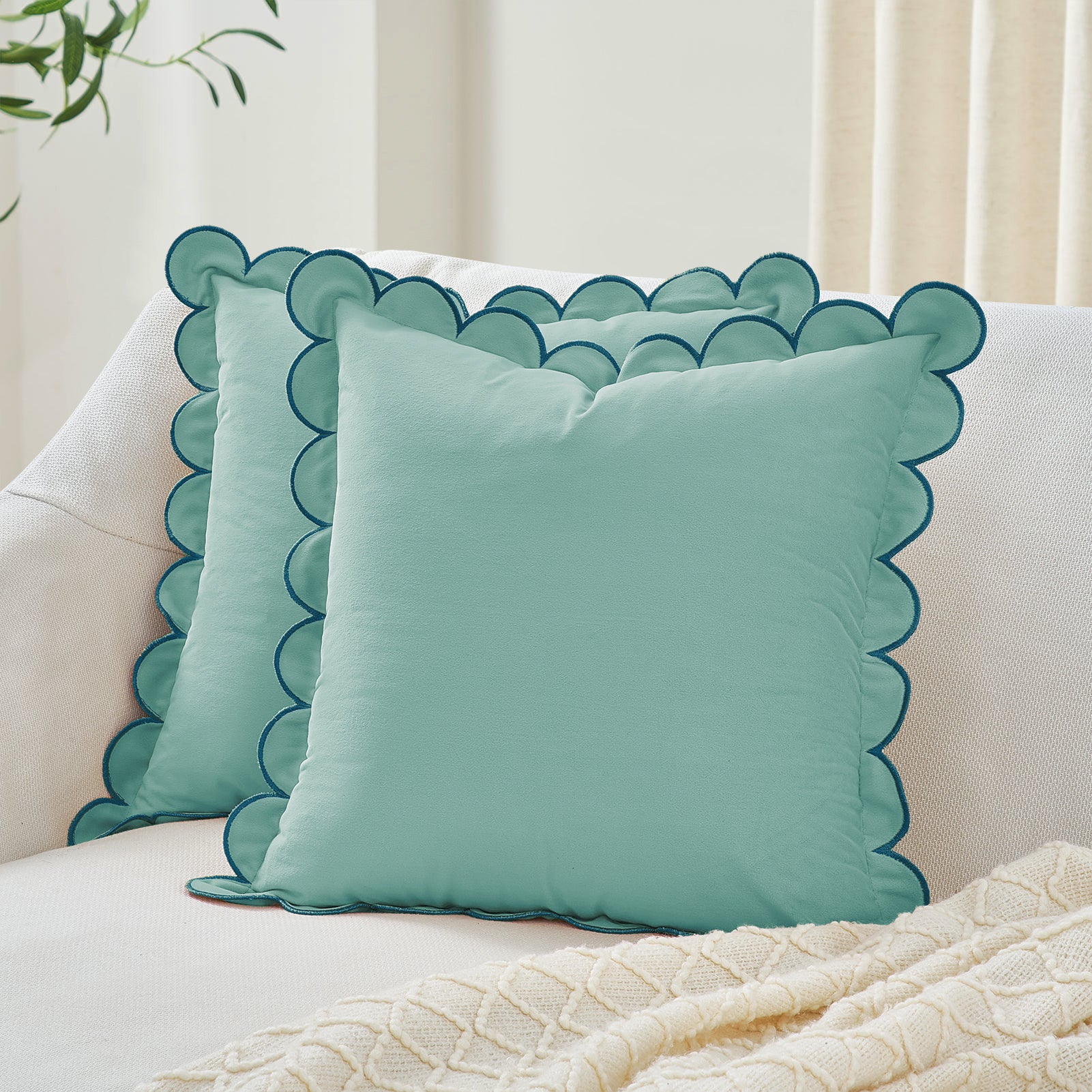 Teal decorative pillows with scalloped edges on a white sofa.
