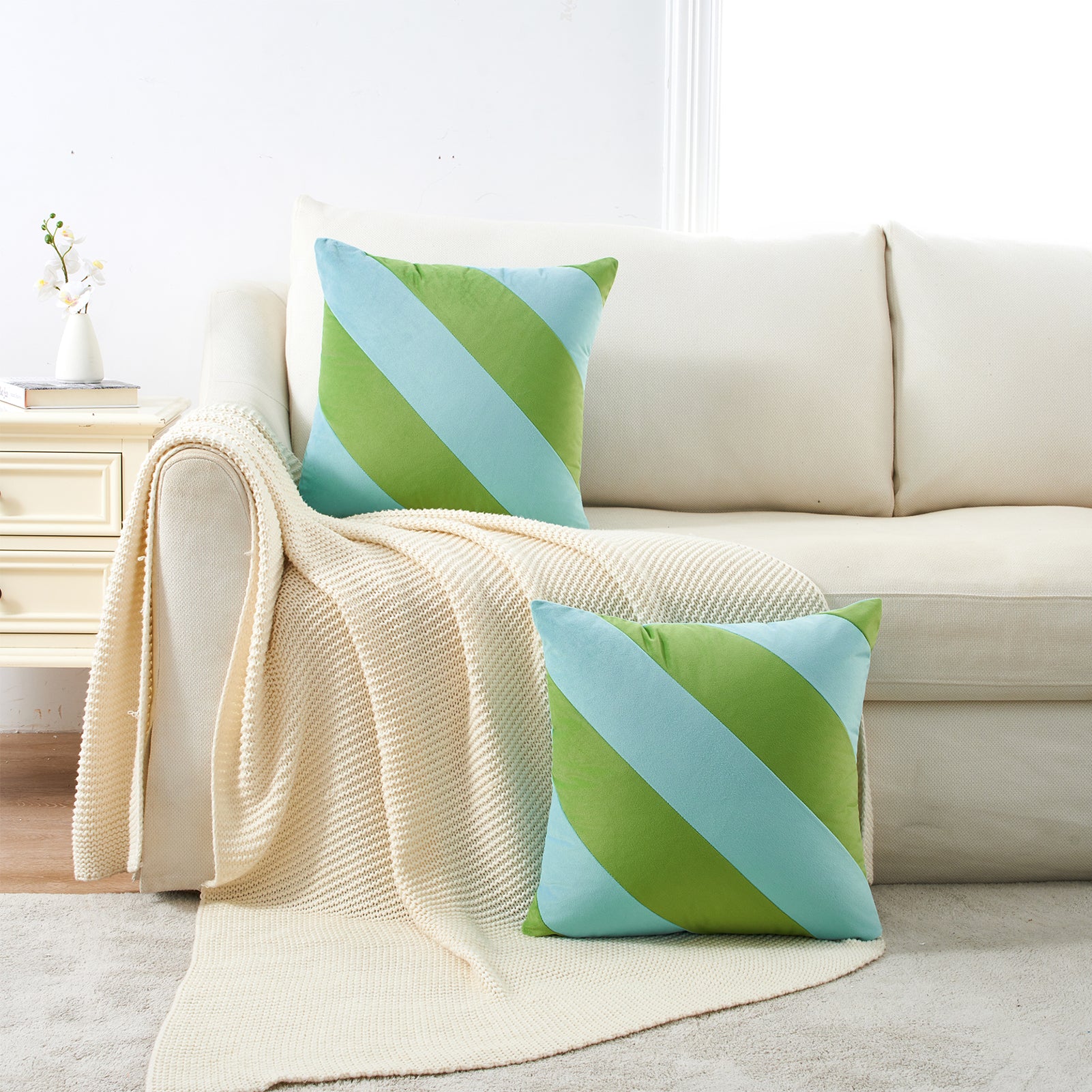 Green and blue striped pillows on a beige sofa with a blanket