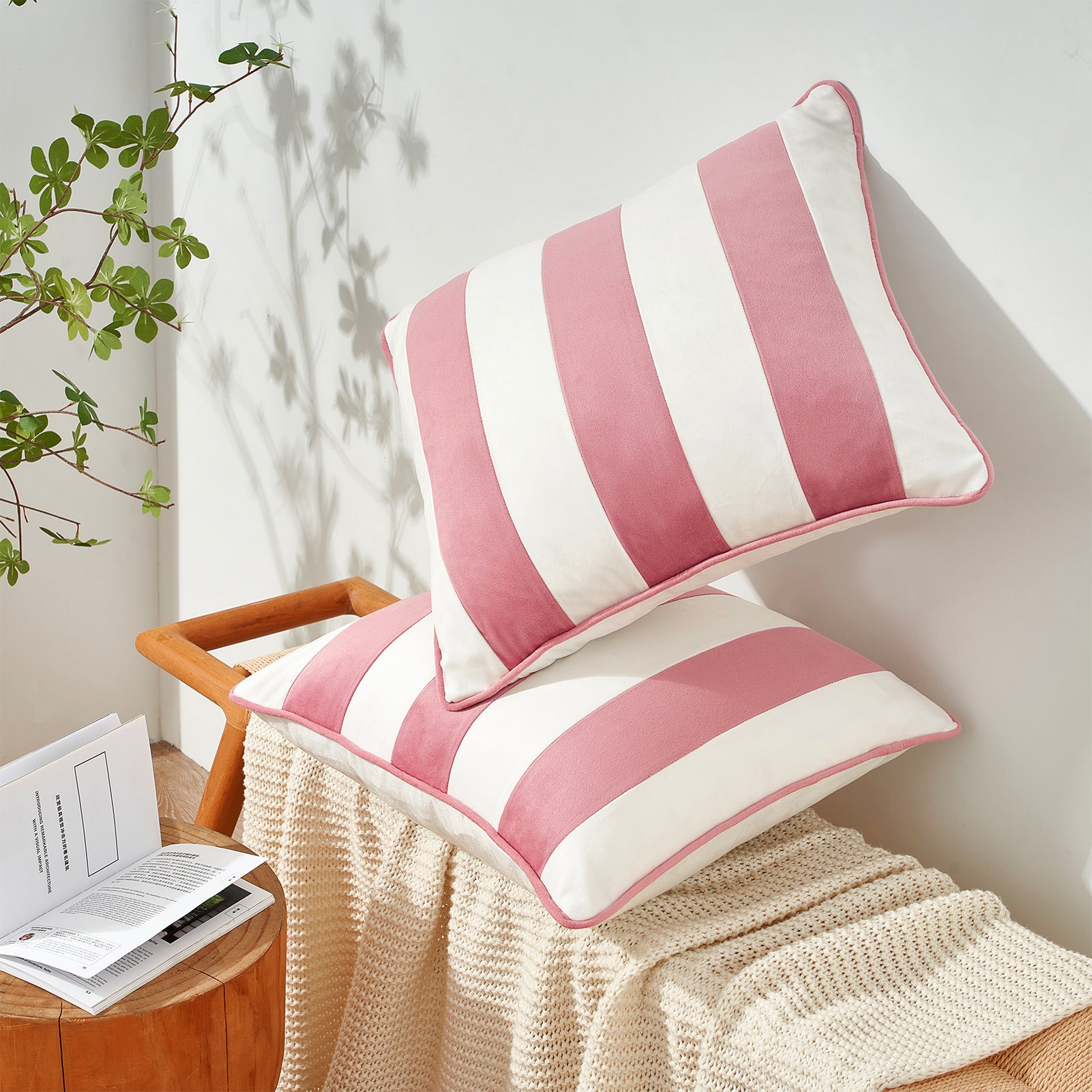Pink and white striped cushions on a wooden chair with a plant and book in the background.