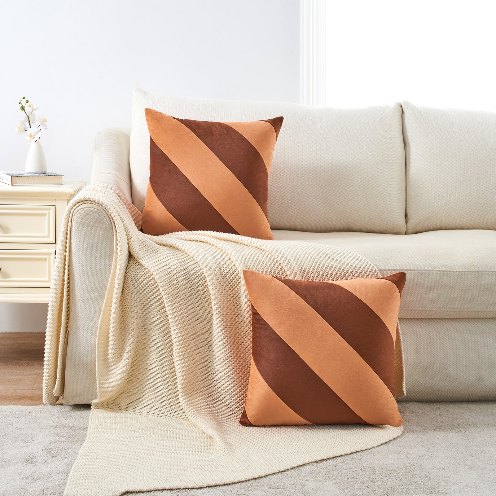 Beige sofa with striped brown and orange cushions and a matching throw blanket.
