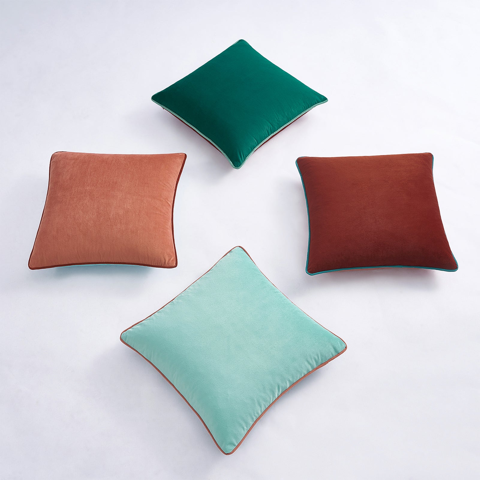 Four square pillows in green, brown, and red on a white background