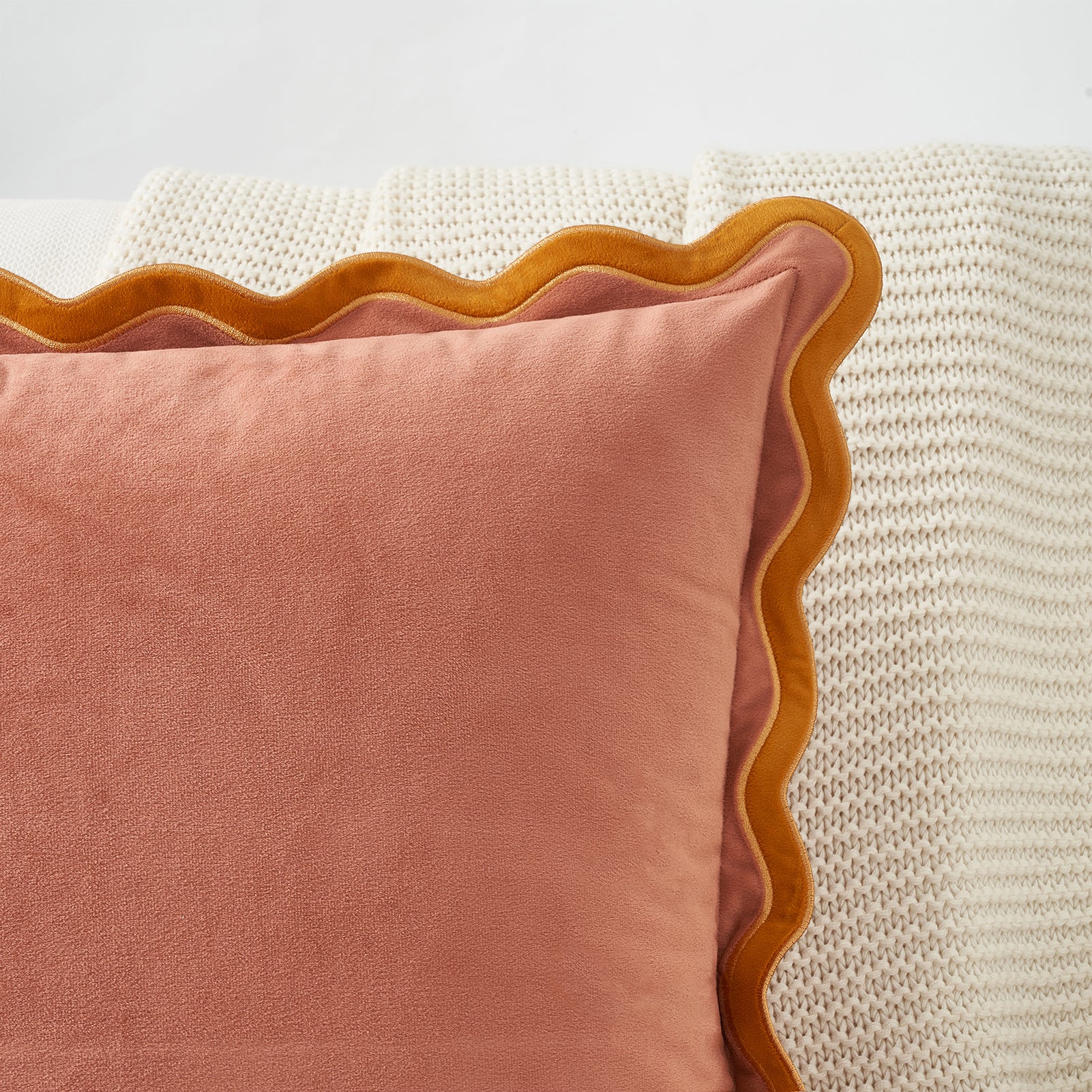 Pink pillow with scalloped edge on a textured surface