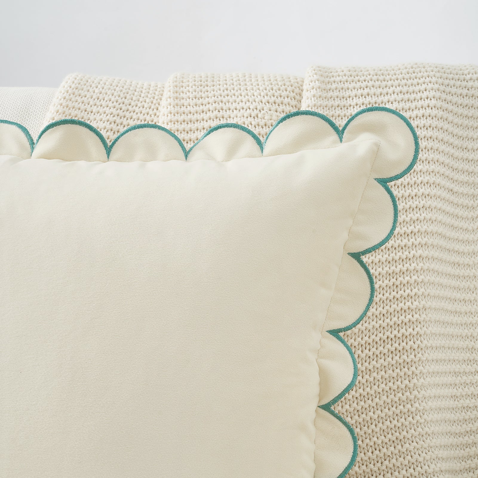 Close-up of a decorative pillow with scalloped edge and teal trim on a textured fabric background.