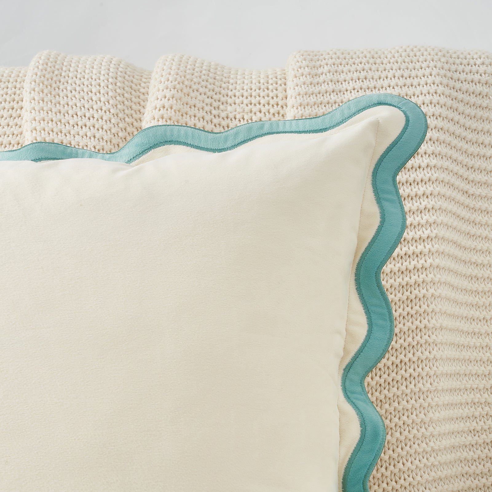 Beige pillow with a wavy blue edge on a textured beige surface