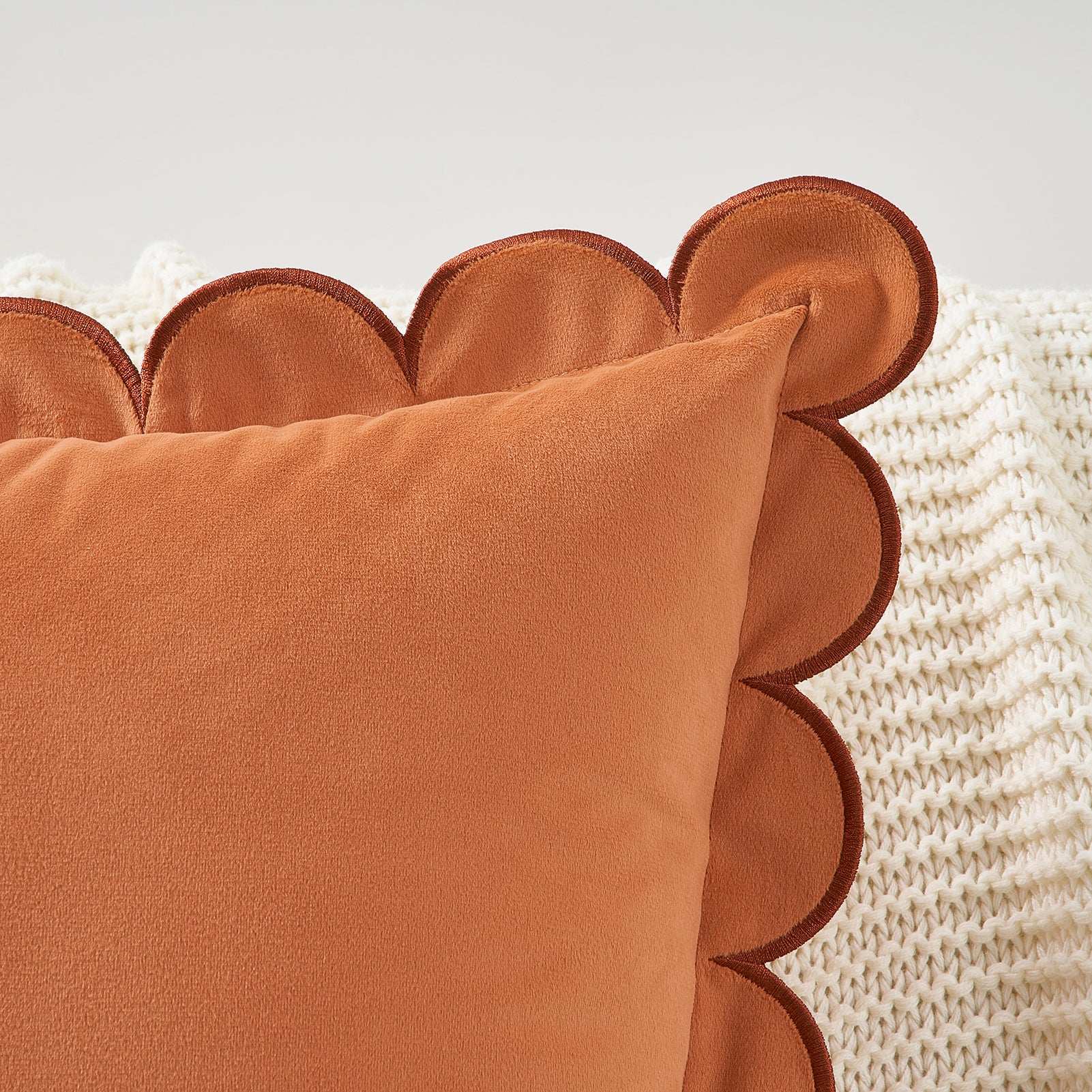 Close-up of a scalloped-edge brown pillow on a textured beige surface