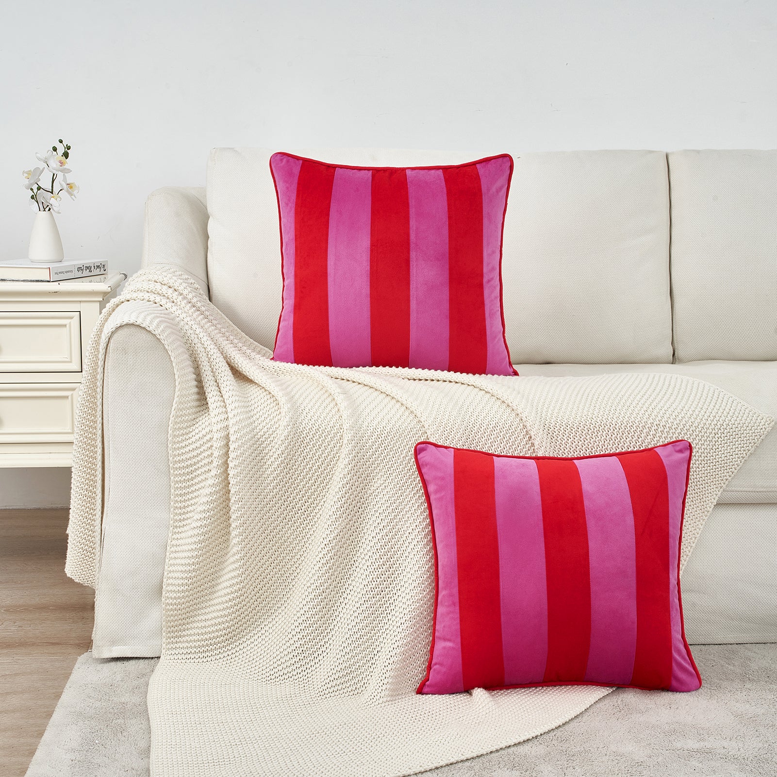 Two red and pink striped pillows on a beige sofa with a white blanket.