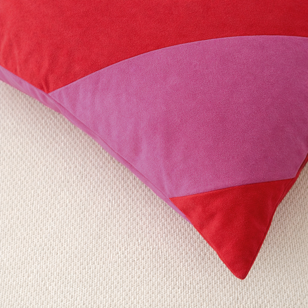 A close-up of a red and pink velvet throw pillow resting on a textured beige fabric surface.