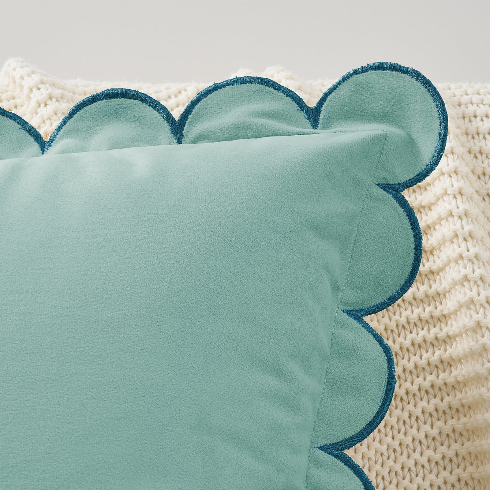 Teal pillow with scalloped edge on a textured beige surface