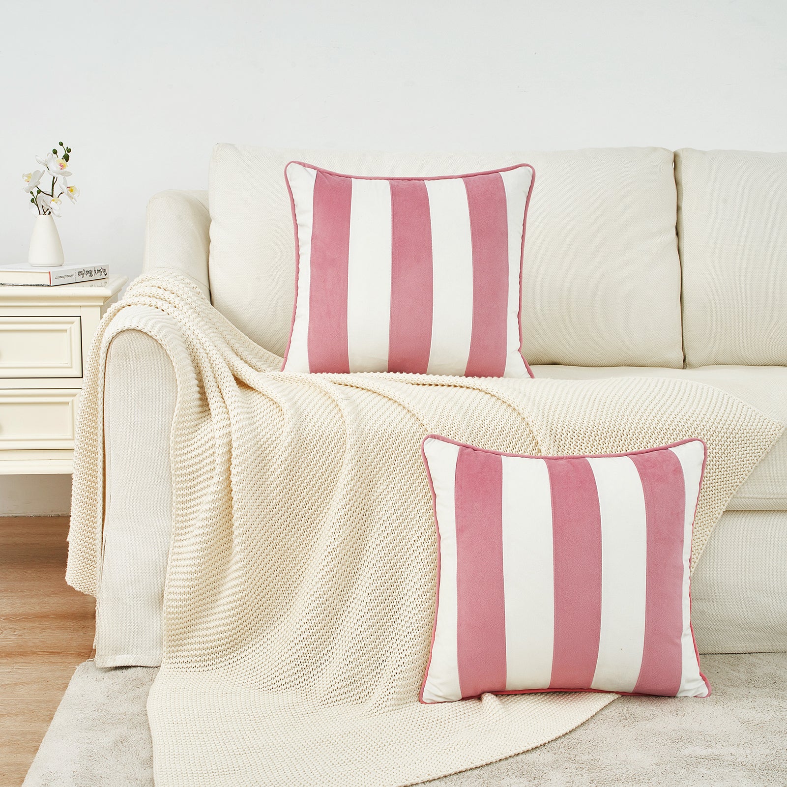 Pink and white striped pillows on a beige sofa with a matching blanket.