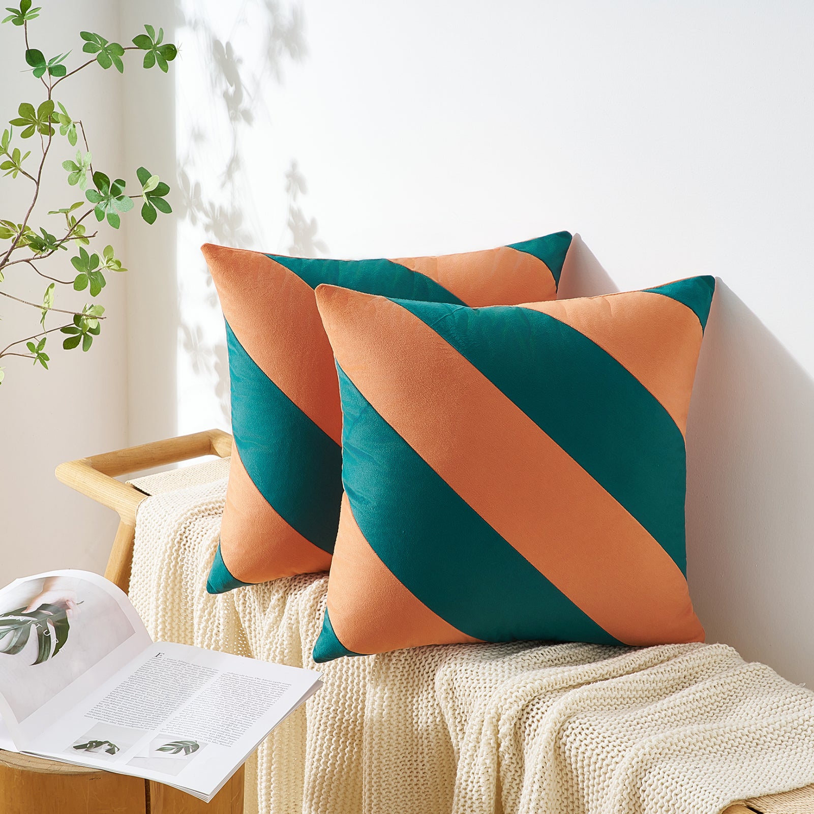 Two decorative pillows with orange and green stripes on a bench with a plant in the background.