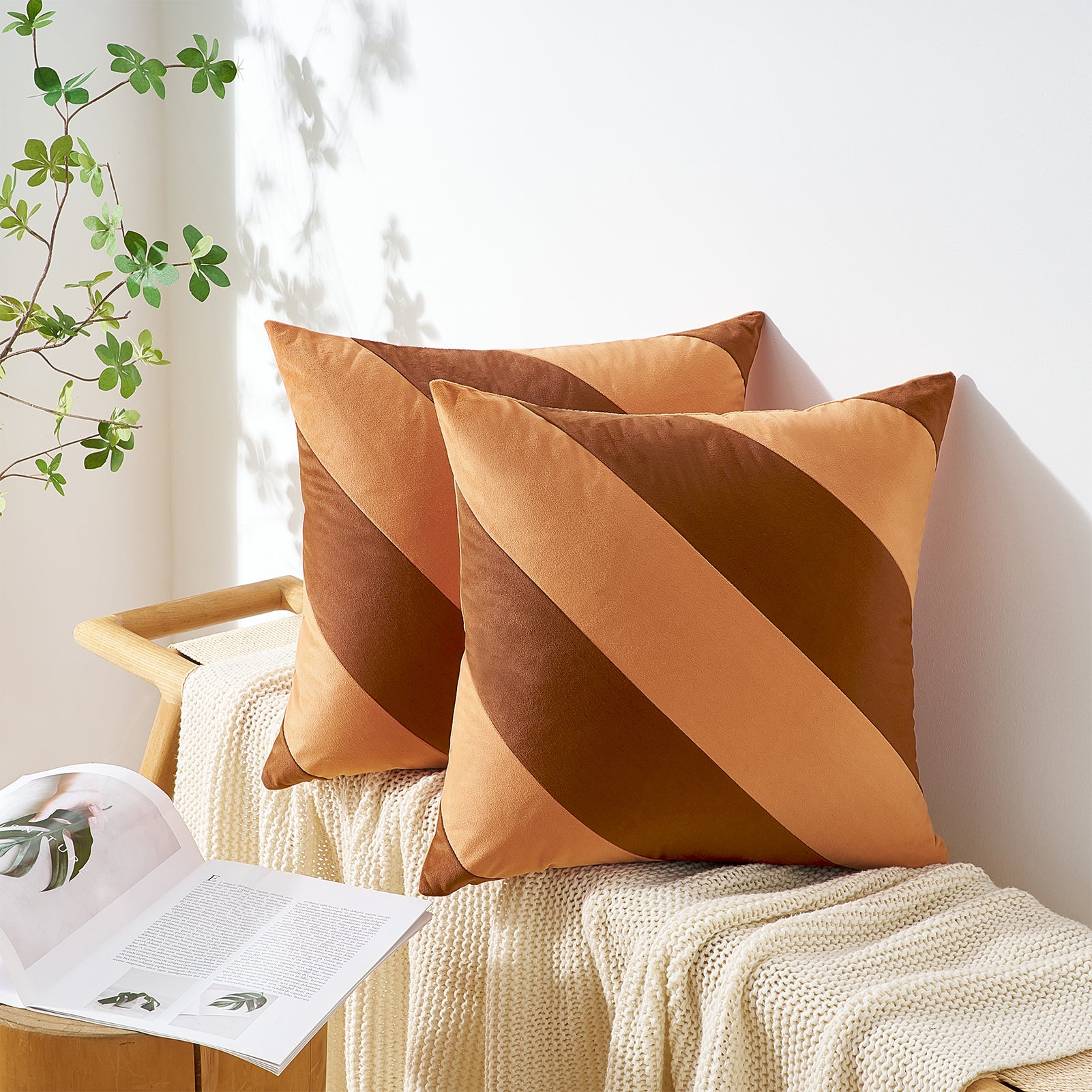 Two brown pillows on a white surface with a plant in the background